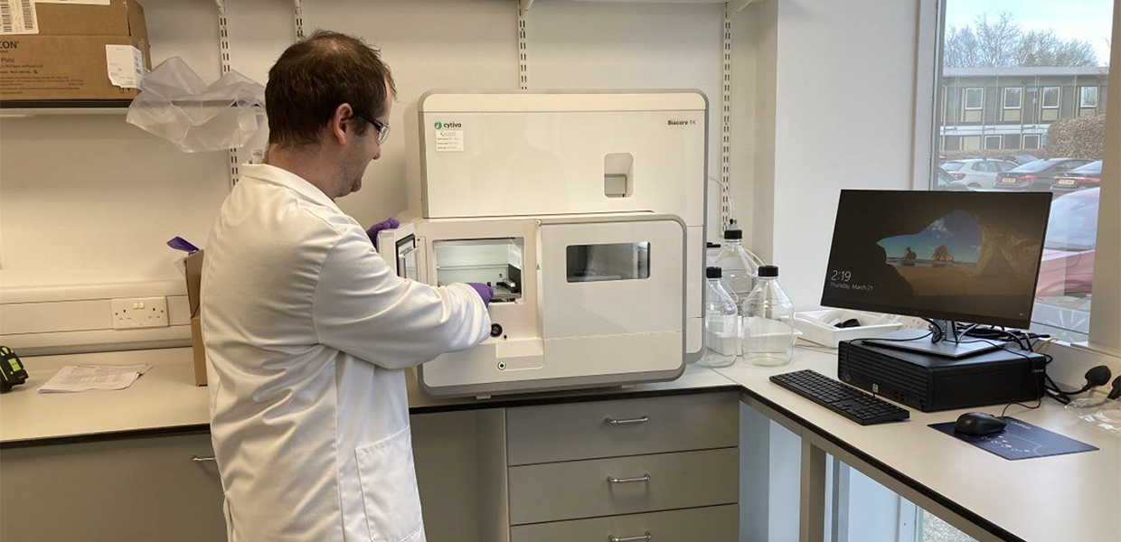 A person in a lab coat and gloves looking at a machine